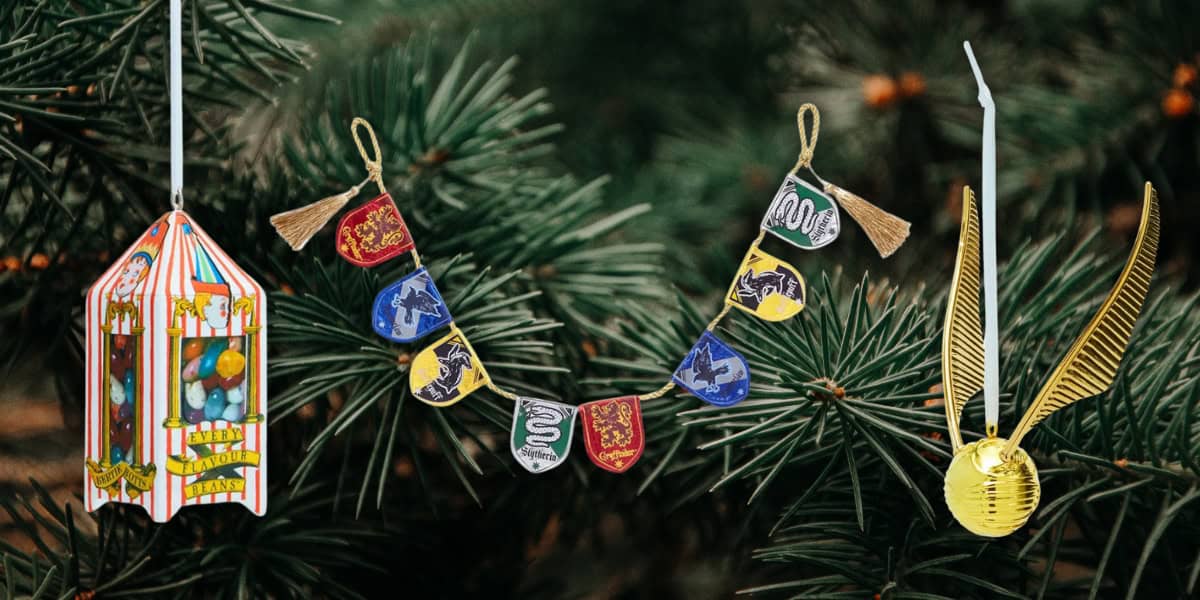 A festive display on a pine branch shows a Honeydukes sweet display, a banner with house crests, and a golden snitch. Each ornament is detailed and colorful, drawing on a magical theme.