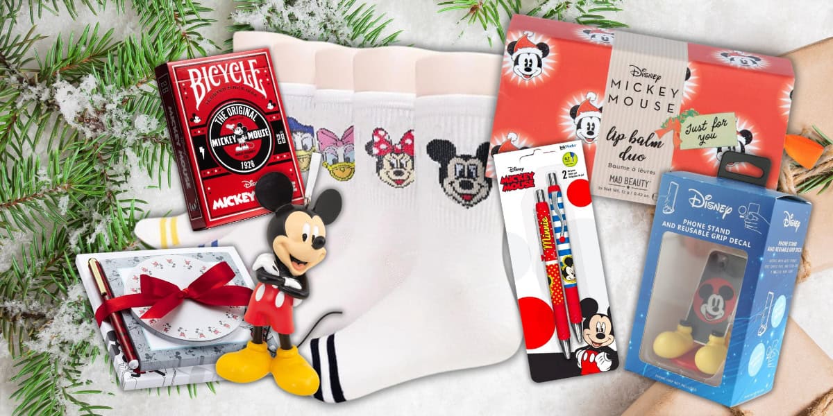 A festive assortment of Disney Mickey Mouse-themed items on snow-dusted ground, including socks, lip balm, playing cards, a figurine, stationery, and a phone stand.