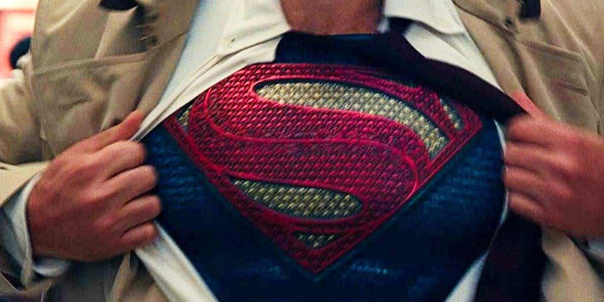 A person wearing a beige trench coat and a white dress shirt is opening their shirt to reveal a Superman costume with the iconic 'S' symbol underneath, reminiscent of Henry Cavill's unforgettable portrayal.