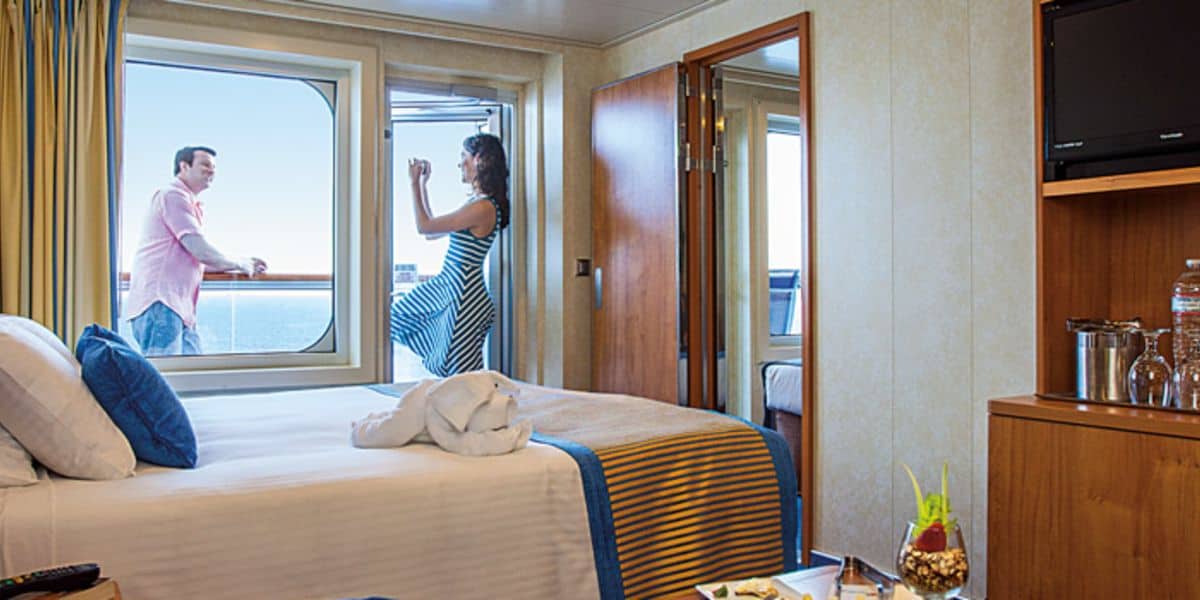 A couple enjoys the view from the balcony of a cruise ship cabin.