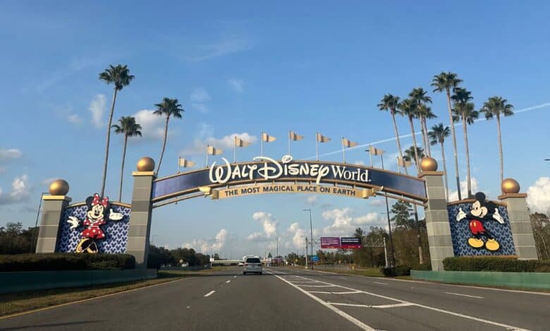 A road leads to the entrance of Walt Disney World featuring a large archway with gold flags. Mickey and Minnie Mouse are depicted on either side.