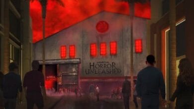 People walk toward a haunted house attraction titled "Universal Horror Unleashed." The building has a spooky, red-lit exterior with glowing windows and eerie fog. The sky above is ominously red, enhancing the horror theme at Universal Horror Unleashed.