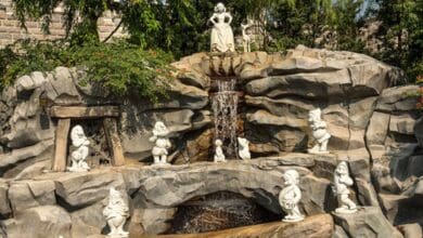 Stone sculptures of Snow White and the Seven Dwarfs grace a rocky waterfall at Snow White Grotto in Disneyland Park.