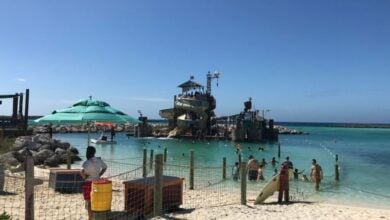 A tropical beach scene at Castaway Cay features a play structure resembling a ship anchored in the water.