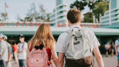 A woman and a man, both with backpacks, walk hand in hand toward the entrance to Disney California Adventure Park.