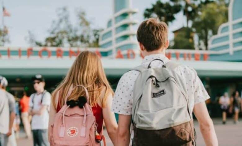 A woman and a man, both with backpacks, walk hand in hand toward the entrance to Disney California Adventure Park.