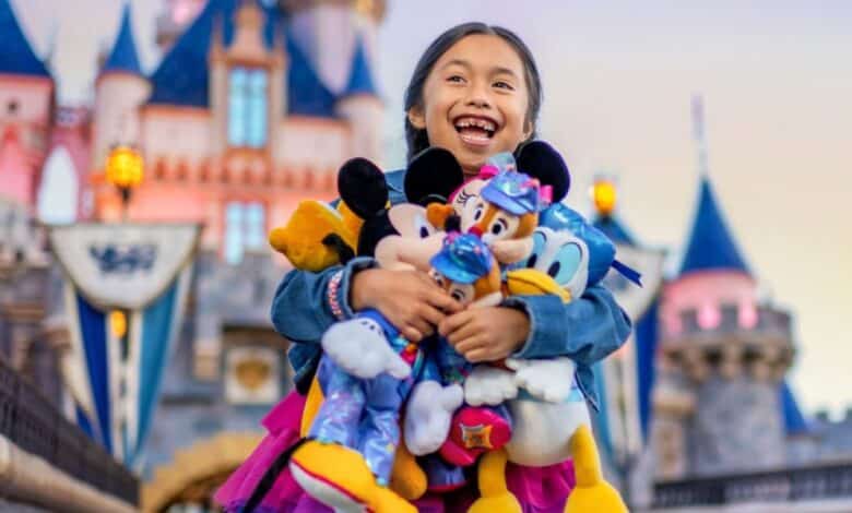 A joyful child holds multiple plush Disney characters, including Mickey, Minnie, and Donald, in front of a colorful fairy-tale castle at a theme park. The background features spires and flags, suggesting a magical atmosphere within Disney World and Disneyland.