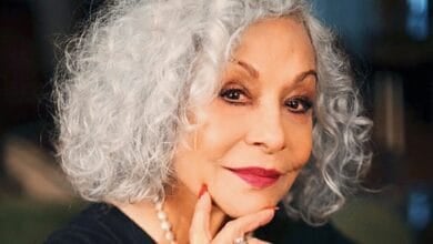 Renee Victor with short, curly gray hair smiles gently at the camera. She is wearing a black top, a pearl necklace, and has her hand resting near her chin with red-painted nails from the hit animated Disney Pixar movie 'Coco'