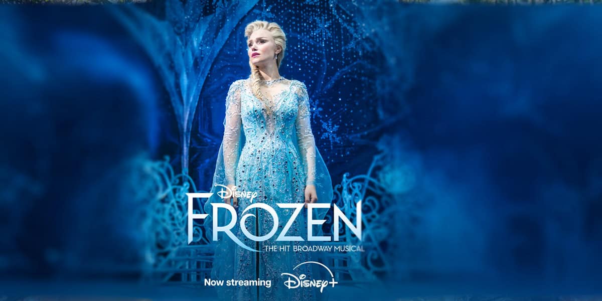 A woman dressed as Elsa in a sparkling blue gown stands onstage with icy blue decorations. Text reads "Disney FROZEN The Hit Broadway Musical. Now streaming Disney+.