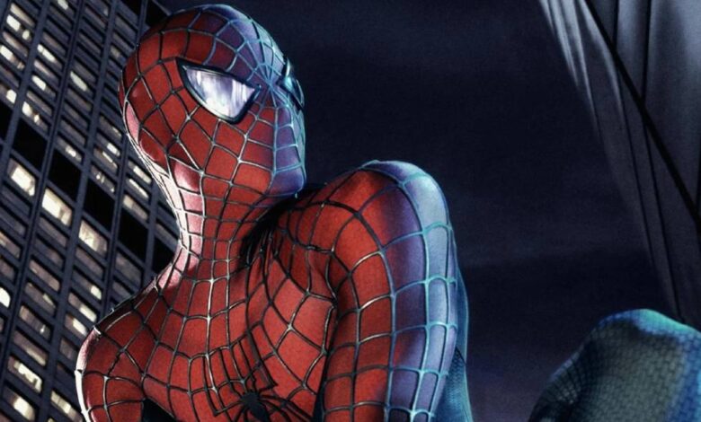 Spider-Man in his red and blue suit crouches on a building at night, looking over his shoulder with city skyscrapers and dark sky in the background.