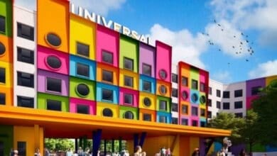 A vibrant, colorful hotel building with square and circular windows, a sign reading "UNIVERSAL" on top, and people gathered outside under a bright yellow canopy. Blue sky and birds are in the background at this new location in Texas.