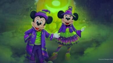 Mickey Mouse and Minnie Mouse wear matching purple and green Halloween costumes at Mickey's Halloween Party.
