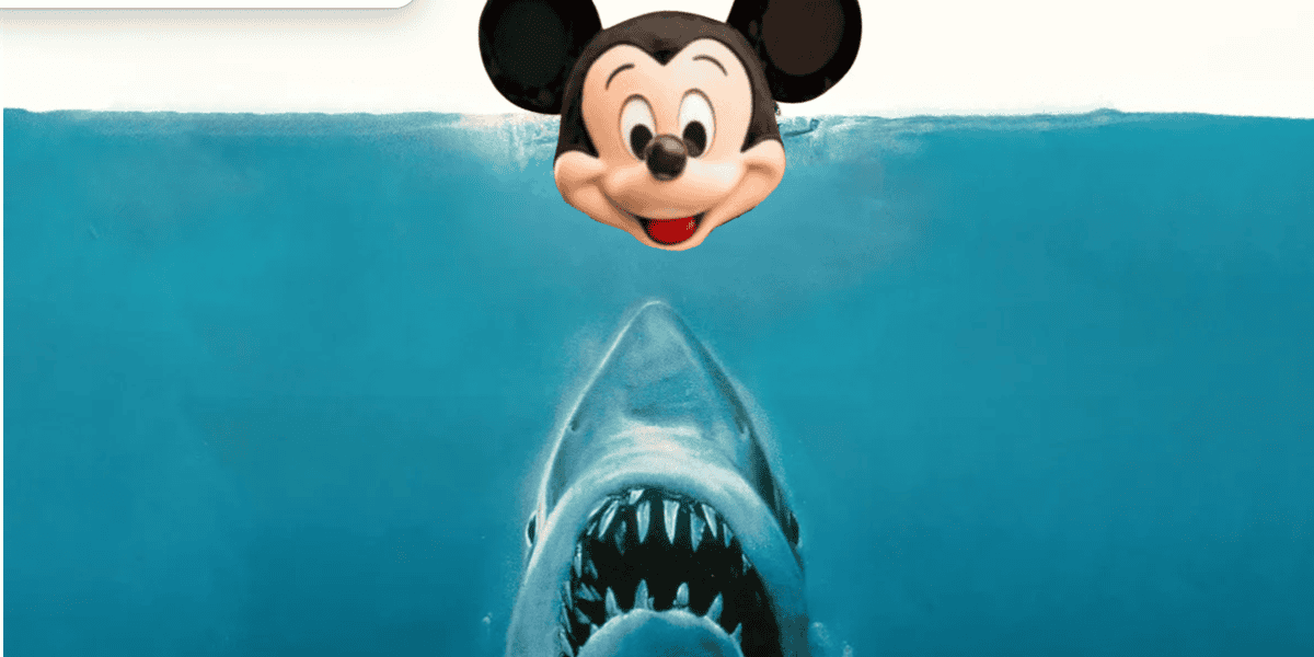 A shark with its mouth open is rising toward the surface of the water, where an illustrated Mickey Mouse head floats above.