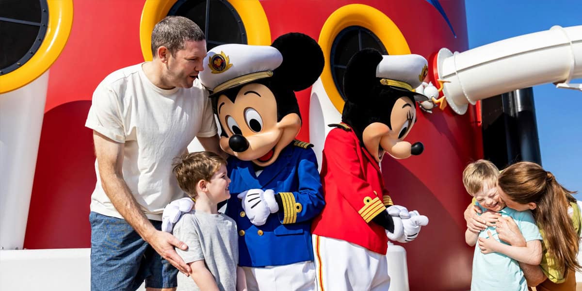 A family with two children meets Mickey and Minnie Mouse in sailor outfits on a cruise ship deck, with bright red and yellow colors in the background.