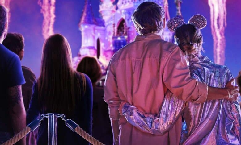 A couple stands in front of Sleeping Beauty Castle watching the fireworks, involving Disney adults at these Disney Parks inside of Disneyland.