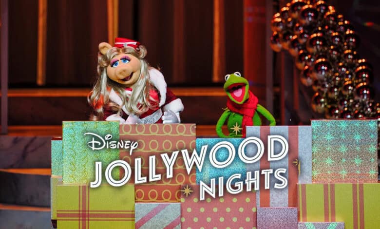Miss Piggy and Kermit the Frog stand behind a stack of colorful presents with a sign reading “Disney Jollywood Nights 2025,” surrounded by holiday decorations and warm lights.