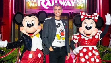 Josh D'Amaro stands between Mickey Mouse and Minnie Mouse in front of "Runaway Railway" ride.