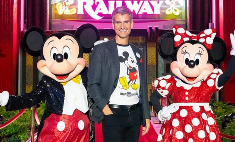 Josh D'Amaro stands between Mickey Mouse and Minnie Mouse in front of "Runaway Railway" ride.