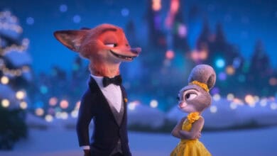 Nick Wilde in a tuxedo and Judy Hopps in a yellow dress stand side by side, smiling at each other, with blurred colorful lights and a castle in the background.