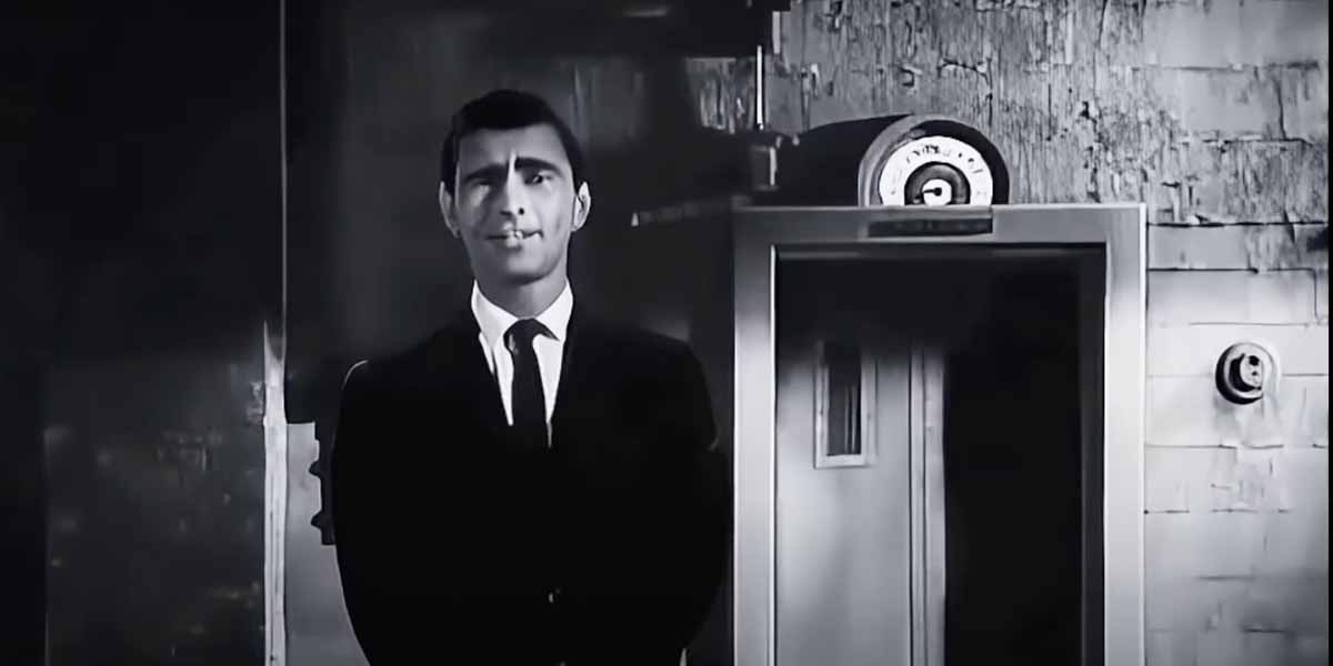 A man in a dark suit and tie stands in front of a door with a circular gauge above it, in a black-and-white setting with a textured wall in the background.