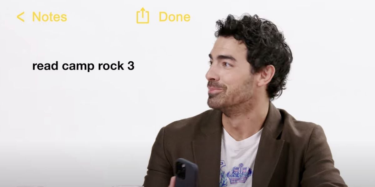 A man with curly dark hair, wearing a brown blazer and holding a phone, looks to the side. On the left, text reads "read camp rock 3" in the style of a Notes app on a white background.