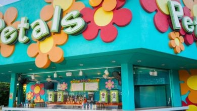 A brightly colored outdoor bar named "Petals" at Pop Century features large, vibrant flower decorations on a turquoise building, with a counter displaying bottles and drink menus visible inside.