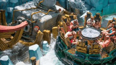 A group of people ride a circular raft on a water rapids attraction at Universal, surrounded by rocks, splashing water, and colorful themed decor.