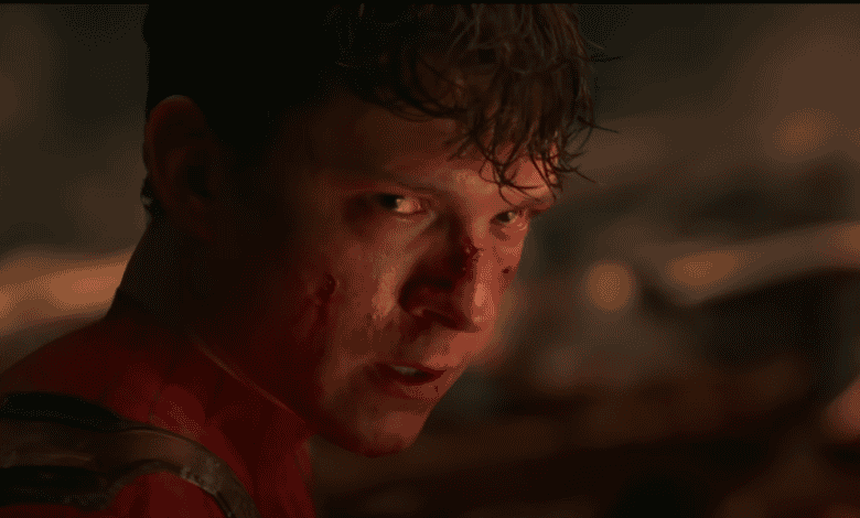 A young man in a red superhero suit, with cuts and blood on his face, looks intensely over his shoulder in a dark, smoky setting.
