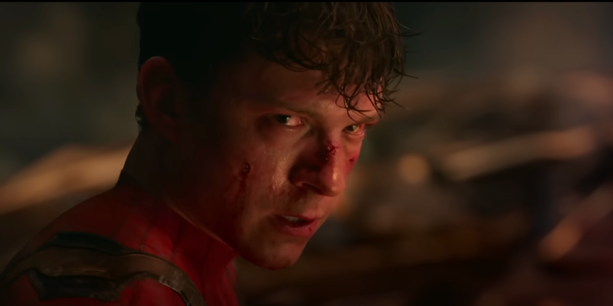 A young man in a red superhero suit, with cuts and blood on his face, looks intensely over his shoulder in a dark, smoky setting.