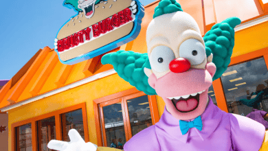 A person in a Krusty the Clown costume stands smiling and waving in front of a bright orange Krusty Burger fast-food restaurant, ready to greet guests at Horror Nights beneath the large cartoon burger sign overhead. Universal Orlando classic attractions closing