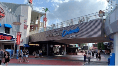 People walk beneath a large sign reading "Welcome to Universal Orlando Resort" at the entrance to Universal, with restaurants like Bubba Gump Shrimp Co. visible on either side.
