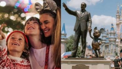 A happy family enjoys Christmas at a theme park, with bright lights in the background. Next to them is a statue of Walt Disney holding hands with Mickey Mouse in front of a castle.