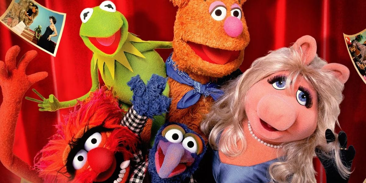 Five colorful Muppet characters, including Kermit the Frog, Fozzie Bear, Miss Piggy, Gonzo, and Animal, pose together in front of a red curtain with photos pinned in the background.