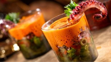 Two glasses filled with a colorful seafood salad worthy of a Disney feast, topped with bright orange sauce and garnished with a cooked octopus tentacle and parsley. The vibrant mix features chopped vegetables and olives.