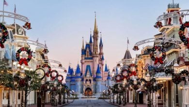 A view of Main Street at Disney World decorated with festive Christmas wreaths and garlands, leading up to the iconic Cinderella Castle under a clear sky.