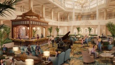 A grand hotel lobby with elegant decor, large chandeliers, a central piano, and a gazebo-style bar overlooks the nearby monorail, as guests relax on sofas among lush green plants in a spacious, sunlit setting.