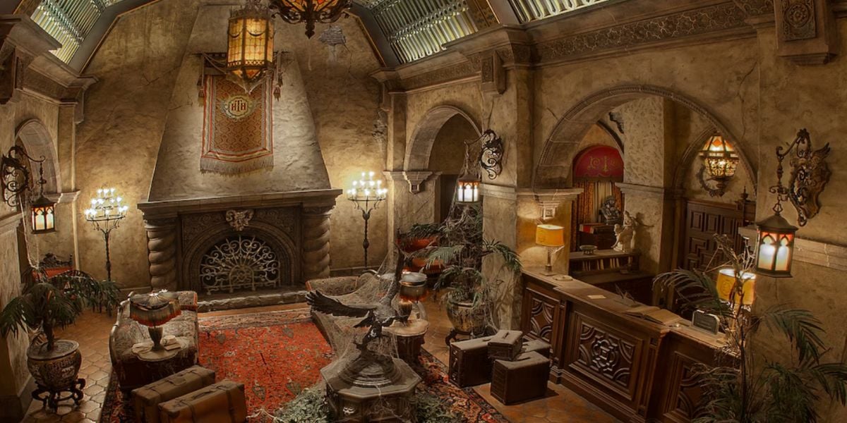 A grand, old-fashioned hotel lobby with ornate furniture, a large fireplace, antique decor, and a red-patterned rug exudes an abandoned, eerie atmosphere reminiscent of the Tower of Terror.