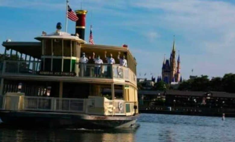 A ferryboat named "Admiral Joe Fowler" crosses a lake with passengers on board, American flags flying, and Cinderella Castle visible in the background under a blue sky. Magic Kingdom ferry boat expansion