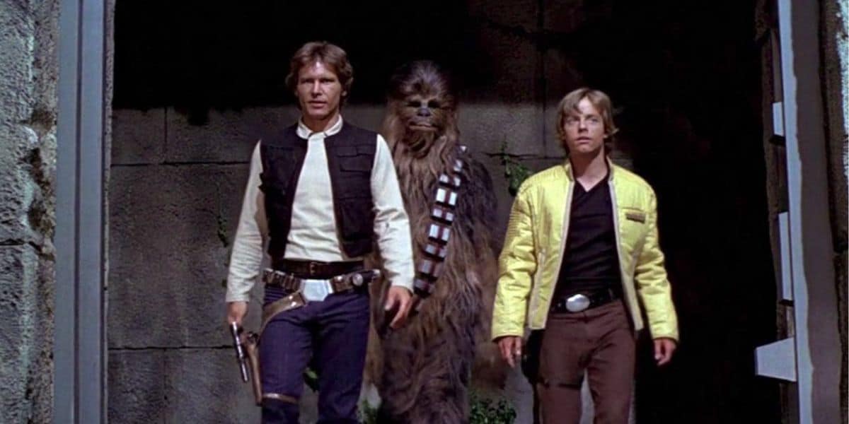 Three characters from Star Wars—Han Solo, Chewbacca, and Luke Skywalker—walk together through a stone doorway. Han holds a blaster, Chewbacca is tall and furry, and Luke wears a yellow jacket in this iconic Star Wars scene.