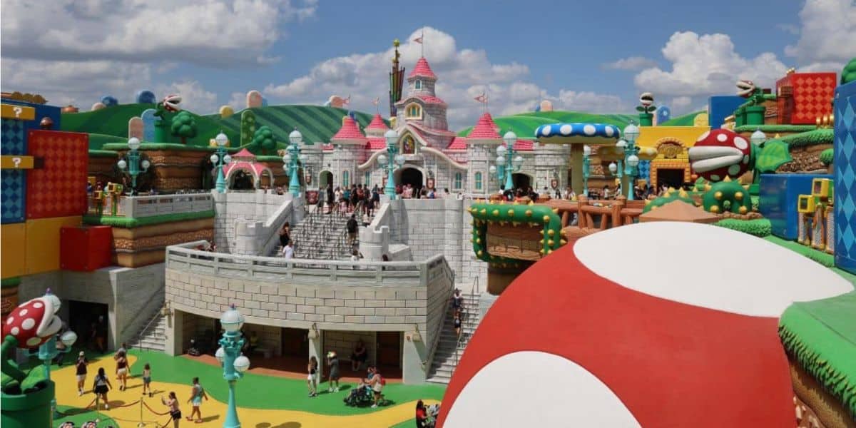A colorful theme park area in Epic Universe inspired by Super Mario features a large red and white mushroom, castle, green hills, and various block structures with visitors walking around.