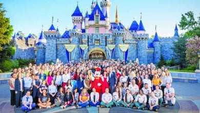 Disney cast members pose with Mickey Mouse in front of Sleeping Beauty Castle at Disneyland Park.