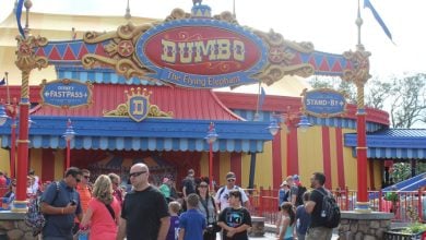 People stand and walk in front of the colorful entrance to “Dumbo the Flying Elephant” ride at Magic Kingdom.