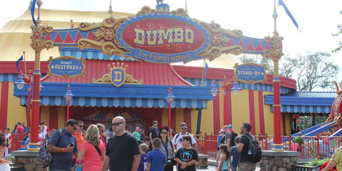 People stand and walk in front of the colorful entrance to “Dumbo the Flying Elephant” ride at Magic Kingdom.