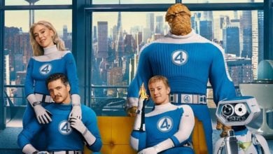 Four people in blue superhero costumes with the number "4" pose together in a city apartment. One is rocky and large, another holds a flame, and a small robot stands beside them. The city skyline is visible through the window.