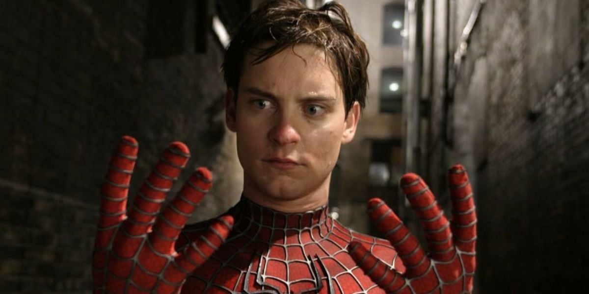 A young man in a Spider-Man suit stands in a dimly lit alley, looking down in surprise at his outstretched gloved hands. His expression is one of shock and disbelief.