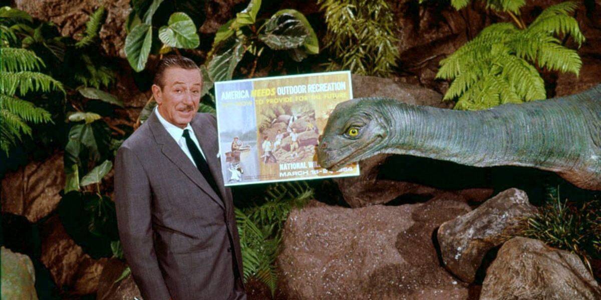 A guest poses by a lifelike dinosaur figure and themed poster, surrounded by tropical plants in a Disney World-style attraction.