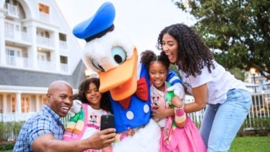 A family of four happily takes a selfie with a person in a Donald Duck costume.