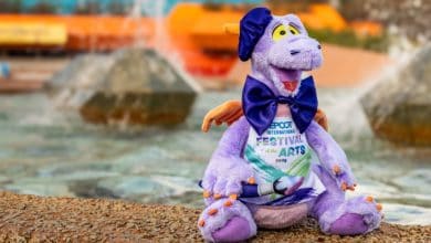 Figment sports a bowtie and festival shirt by the fountain at CommuniCore Hall during EPCOT Festival of the Arts 2026.