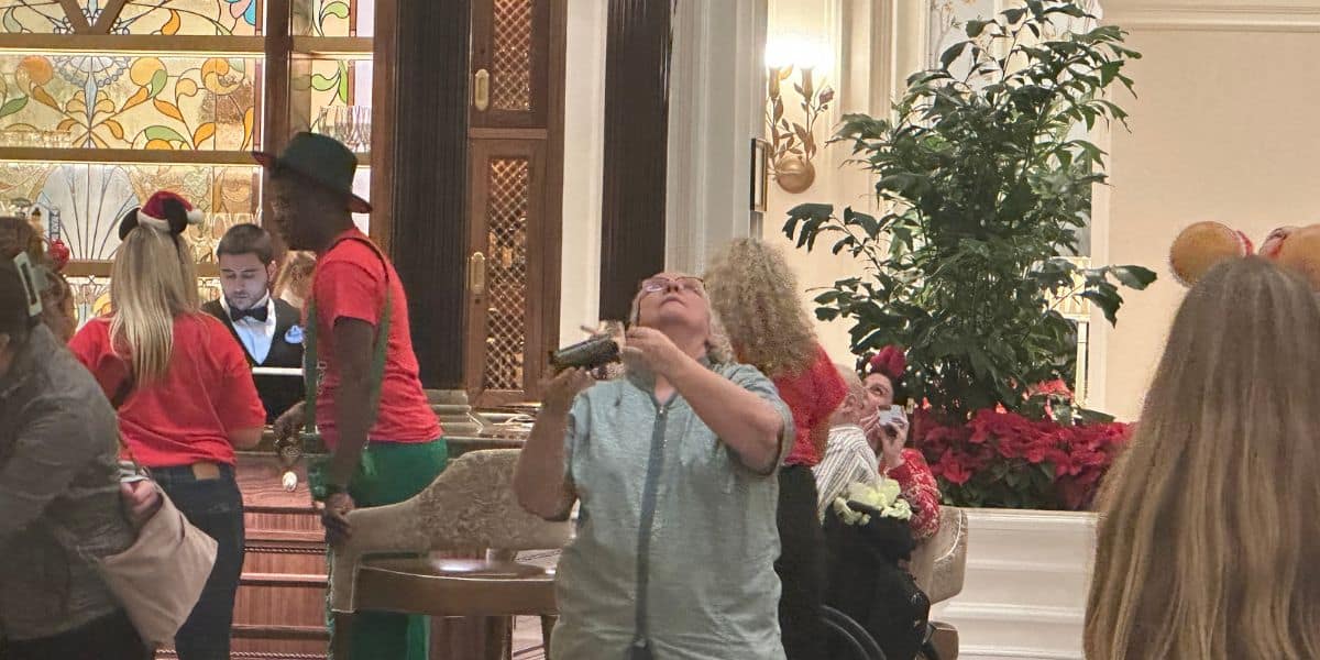 A guest snaps a photo in Disney’s Grand Floridian Resort lobby, surrounded by cast members and visitors in festive holiday outfits.