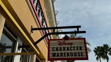Disney Character Warehouse sign welcomes guests outside a vibrant yellow storefront, framed by palm trees and overcast skies.